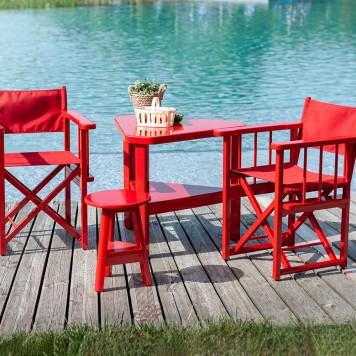 photo en bord d'un lac, sur ponton bois, ensemble de mobilier de jardin en bois laqué rouge. Fauteuils, table et tabouret