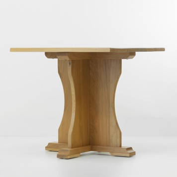 Table en chêne avec pied central en forme de vague vue de profil dans une pièce en fond blanc.